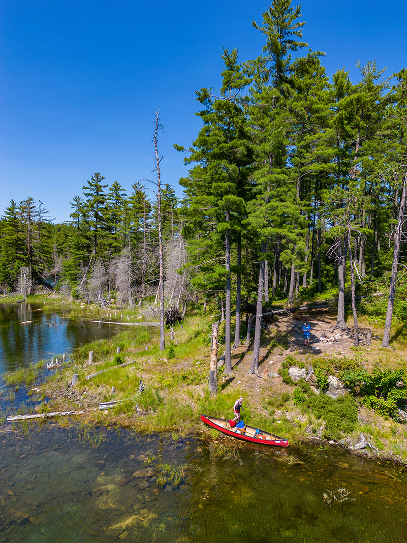 people at a lakeside campsite with a red canoe