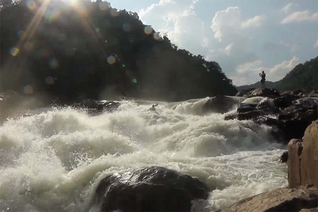 a person films from the rocky shore while another person goes whitewater kayaking in India