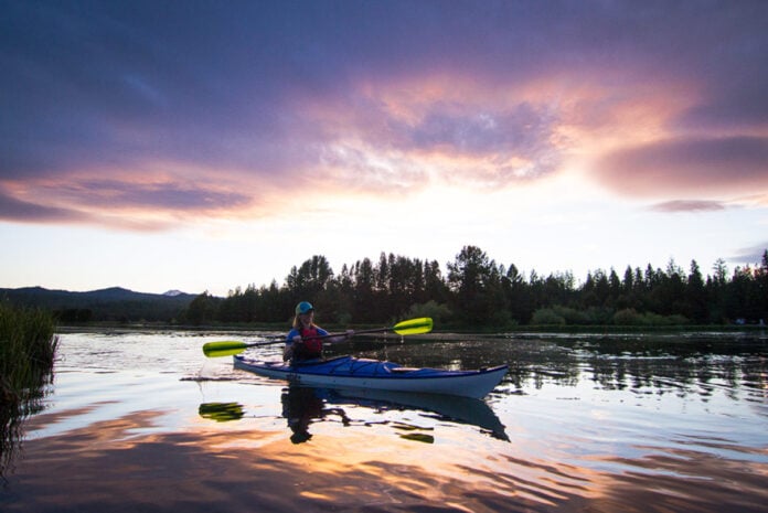 Woman paddling a kayak on a lake at sunset