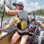 The Beginner’s Guide To Canoeing Pair of paddlers kneeling in a canoe as they go through a rapid.