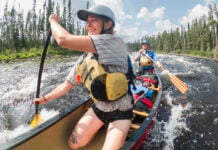 Pair of paddlers kneeling in a canoe as they go through a rapid.