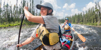 Pair of paddlers kneeling in a canoe as they go through a rapid.