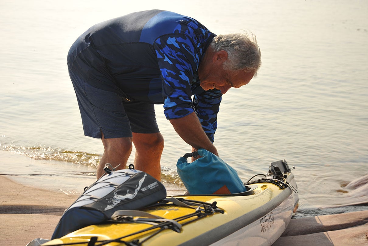 man rummages inside the stern hatch of his sit-inside touring kayak