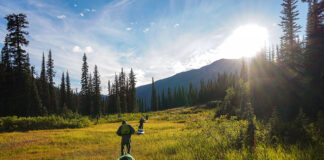 people tow whitewater kayaks on portage through a grassy field in the hills