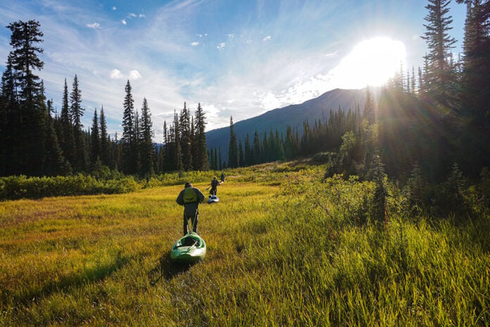people tow whitewater kayaks on portage through a grassy field in the hills