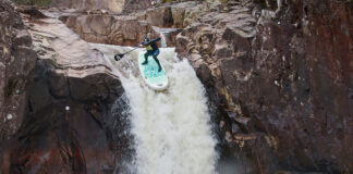 man paddleboards over Right Angle Falls in the Scottish Highlands