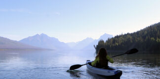 woman paddles an inflatable kayak on a peaceful lake with mountain backdrop