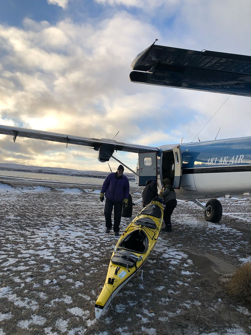 person drags a yellow sea kayak toward a small plane