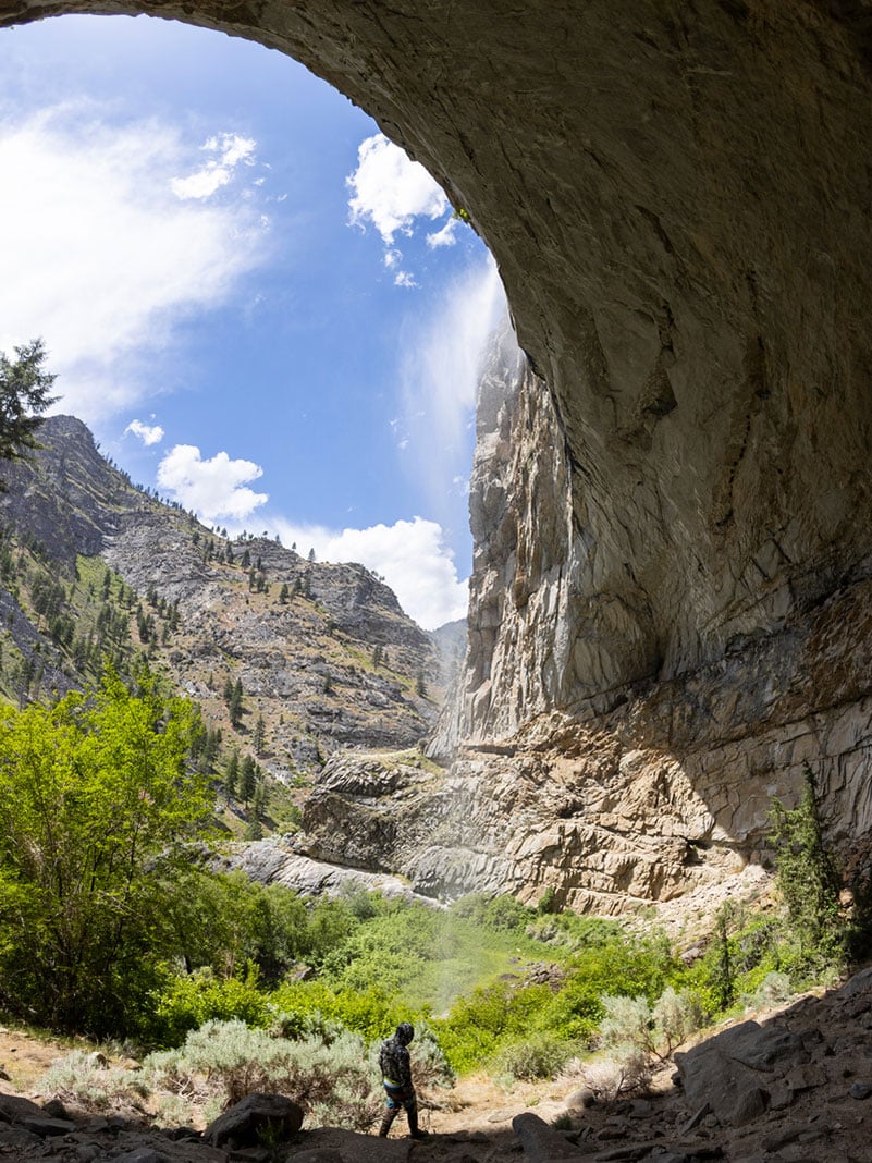 a person hikes past a waterfall under a rocky arch along the Middle Fork of the Salmon River