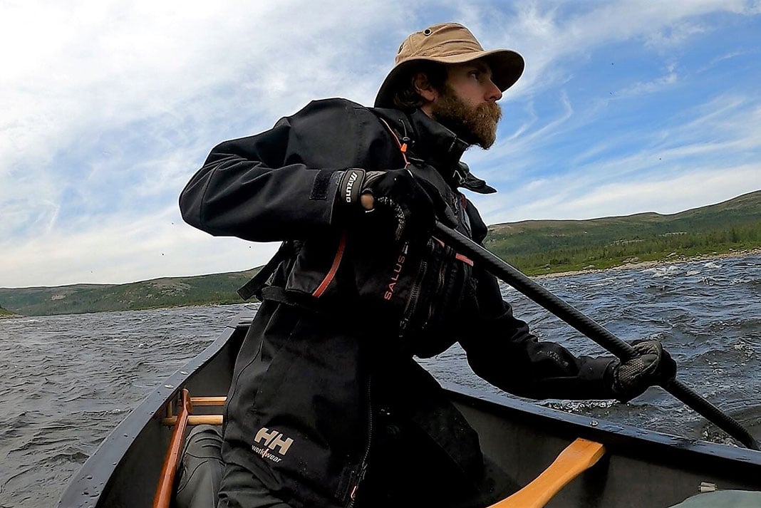 man paddles canoe aggressively on a northern river