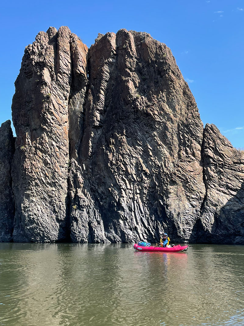 woman kayaks in front of a rocky outcropping in Oregon