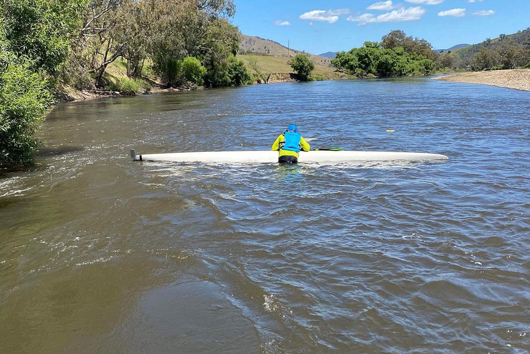 man leans over capsized expedition kayak