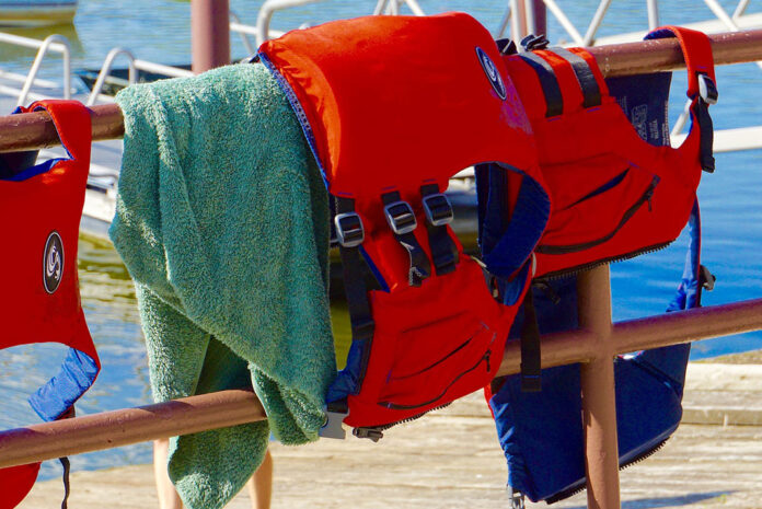 two Stohlquist life jackets hang over a fence with a towel
