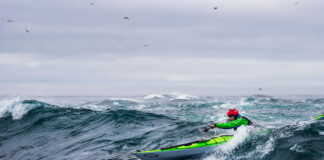 man paddles a Current Designs sea kayak in surf