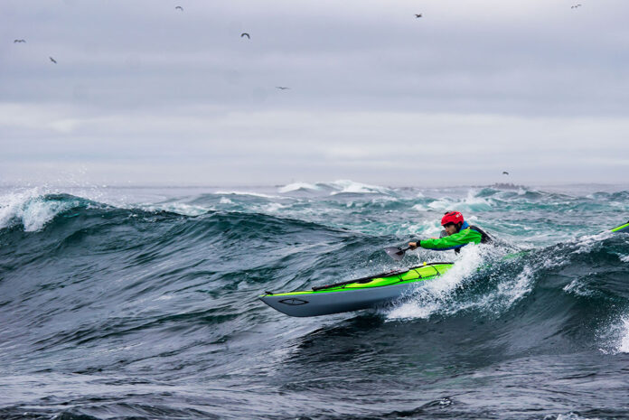 man paddles a Current Designs sea kayak in surf