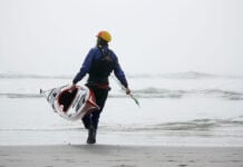 man carries Current Designs Sisu kayak into the water on a beach