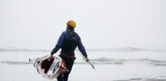 man carries Current Designs Sisu kayak into the water on a beach