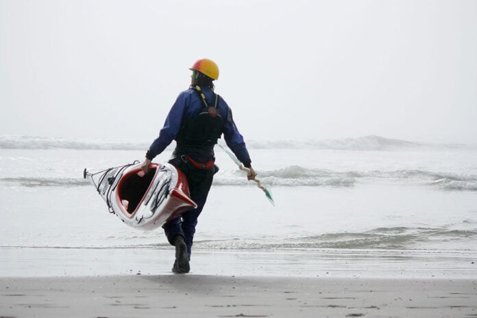 man carries Current Designs Sisu kayak into the water on a beach
