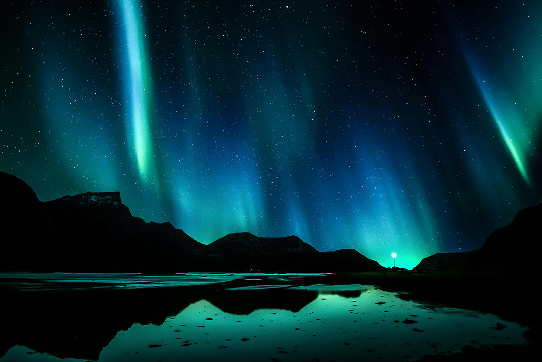 northern lights and mountain silhouettes reflected on water