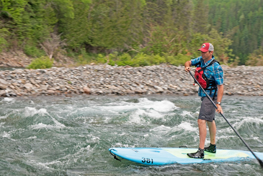 man paddleboards along the Bonaventure River through light rapids in Quebec