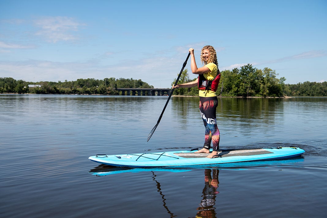 woman stands on a paddle board on a sunny waterway in Quebec