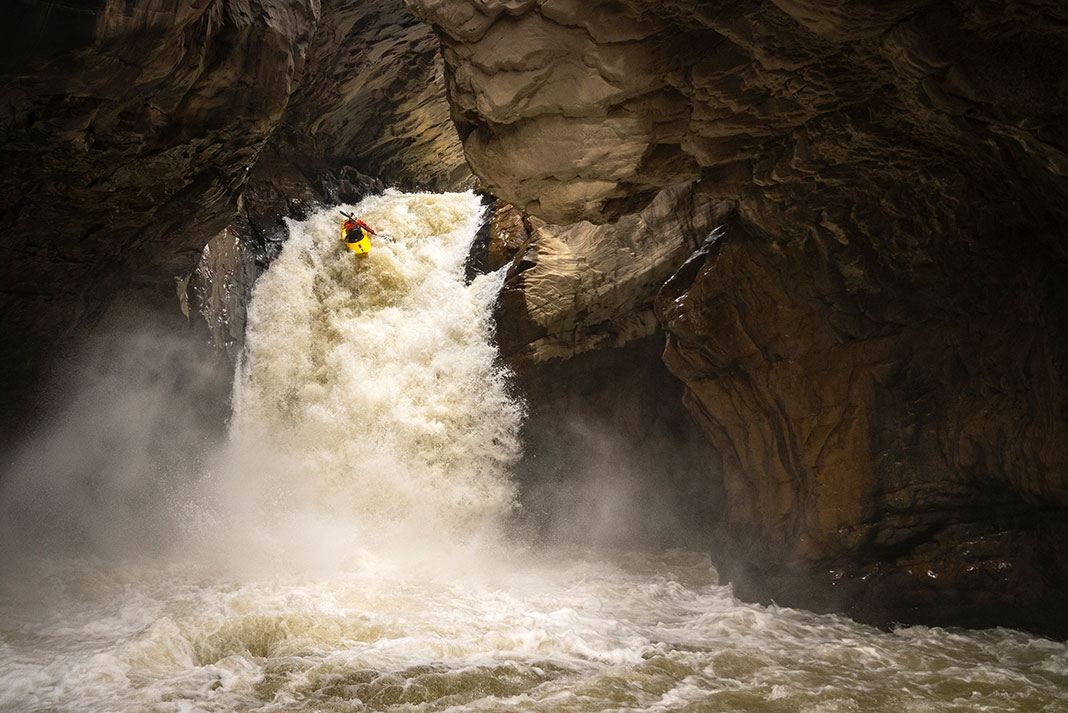 a whitewater kayaker drops off a rushing waterfall in a cavern