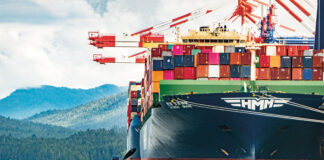 man paddles a kayak in front of a large container ship in British Columbia