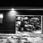black and white photo looking into a garage full of paddling gear at night with garage door open