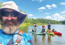 man in bucket hat and PFD takes photo with three kayak anglers posing on boats in the background