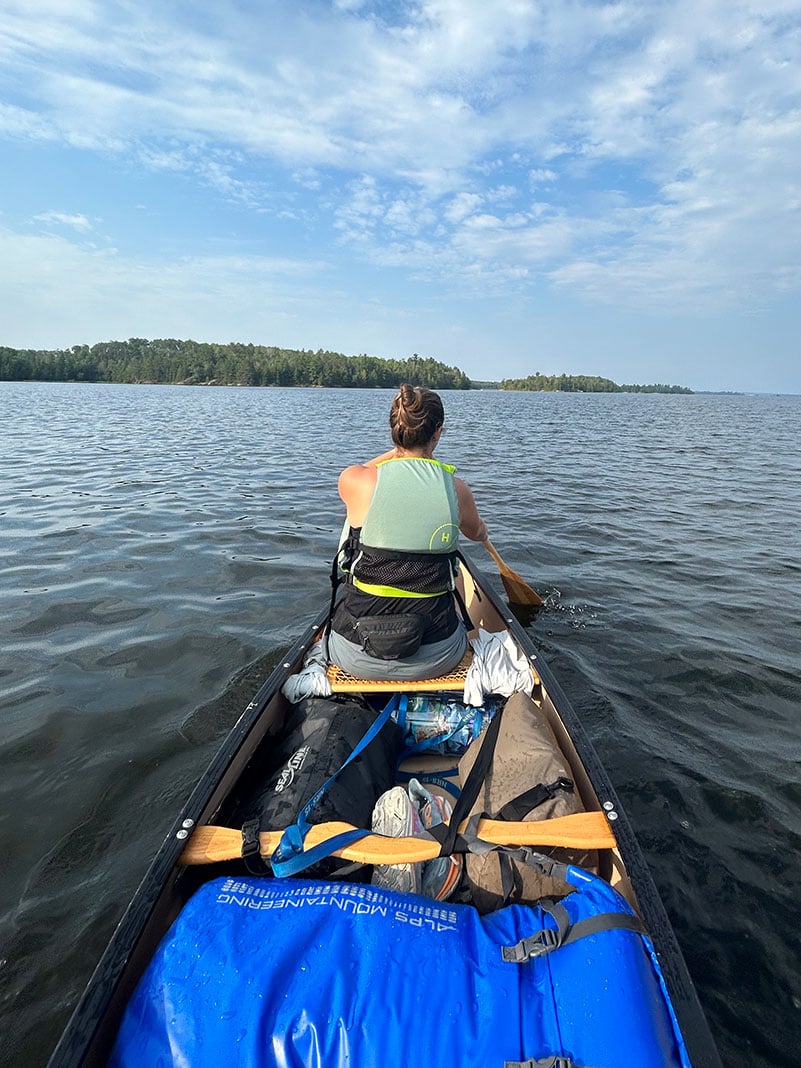 bow shot of woman paddling a laden tripping canoe across a lake in Minnesota