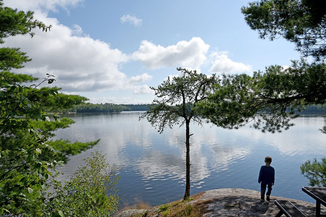 child stands on a rocky outcropping at a campsite overlooking a lake