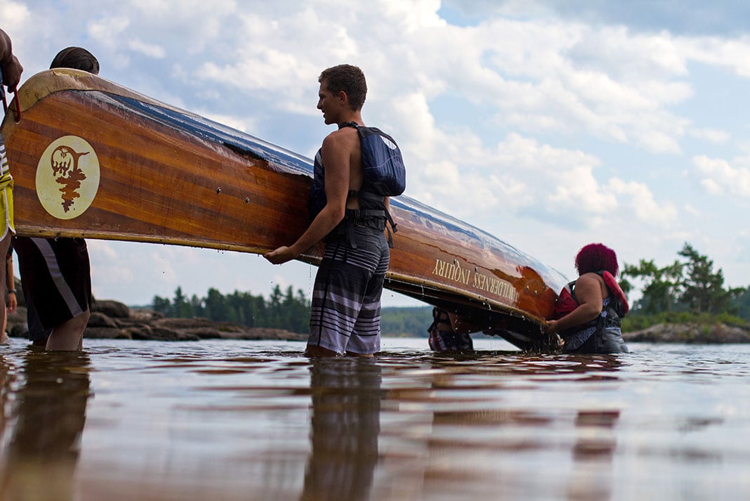 a group of people lift an upturned canoe out of the water