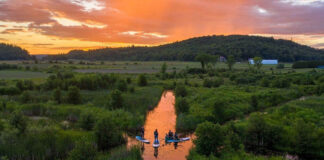 paddleboarders SUP along a sunlit Quebec waterway at dusk