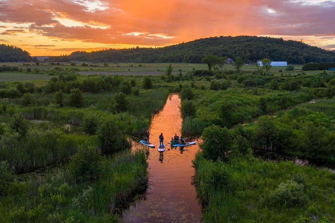 paddleboarders SUP along a sunlit Quebec waterway at dusk