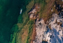 overhead photo of a person paddling an electric sup through blue water past a rocky shelf