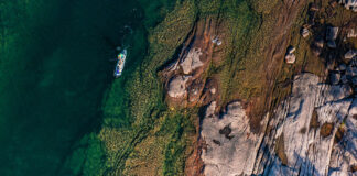 overhead photo of a person paddling an electric sup through blue water past a rocky shelf