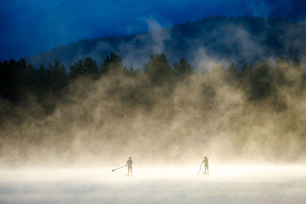 two people paddling paddleboards in the mist