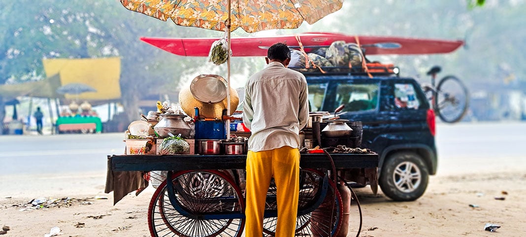 jeep with kayak is parked behind a street vendor's cart in India