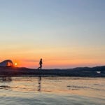 a woman walks around her waterside campsite at dusk while on a microadventure