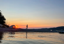 a woman walks around her waterside campsite at dusk while on a microadventure