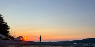 a woman walks around her waterside campsite at dusk while on a microadventure