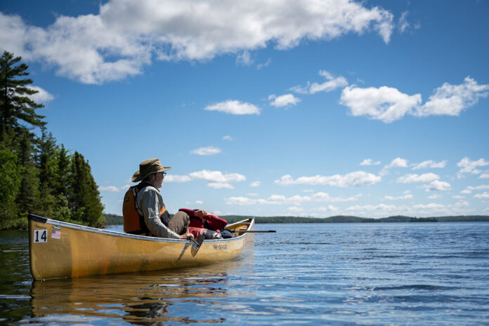 an older man sits in an ultralight canoe and looks out across a northern lake