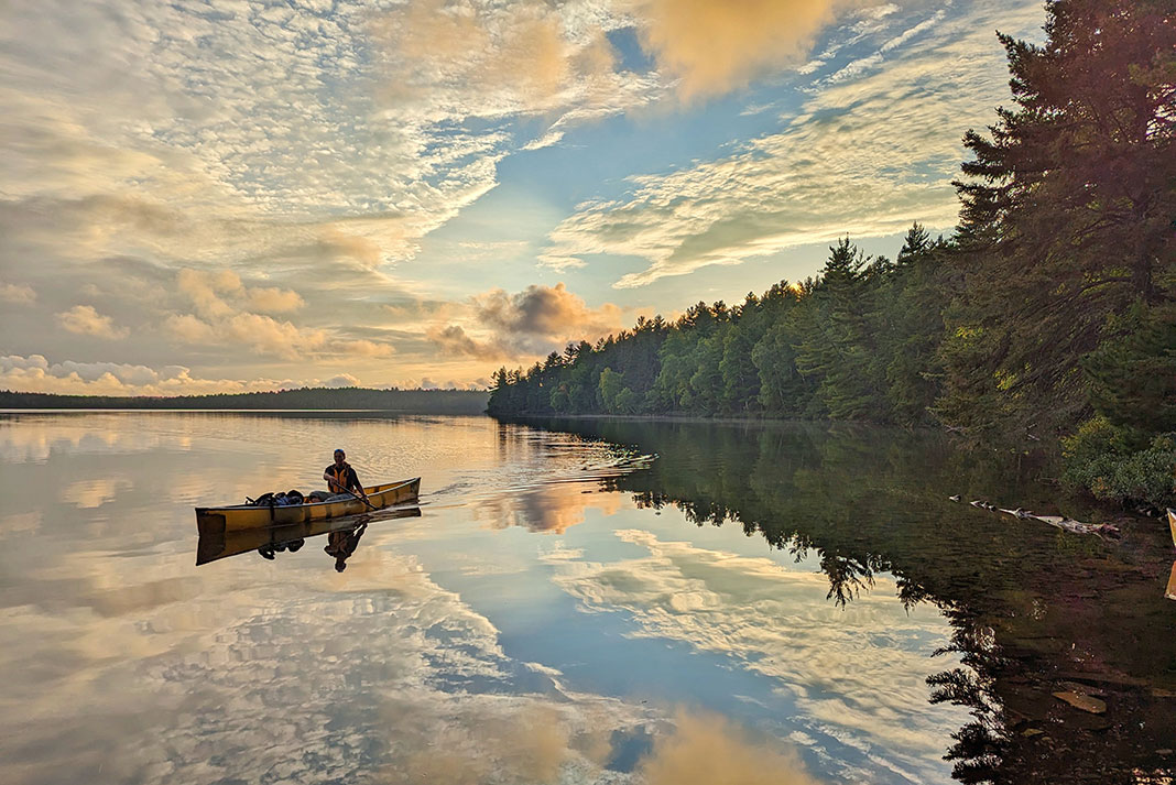 a person paddles a canoe at dusk in front of a misty lake shoreline