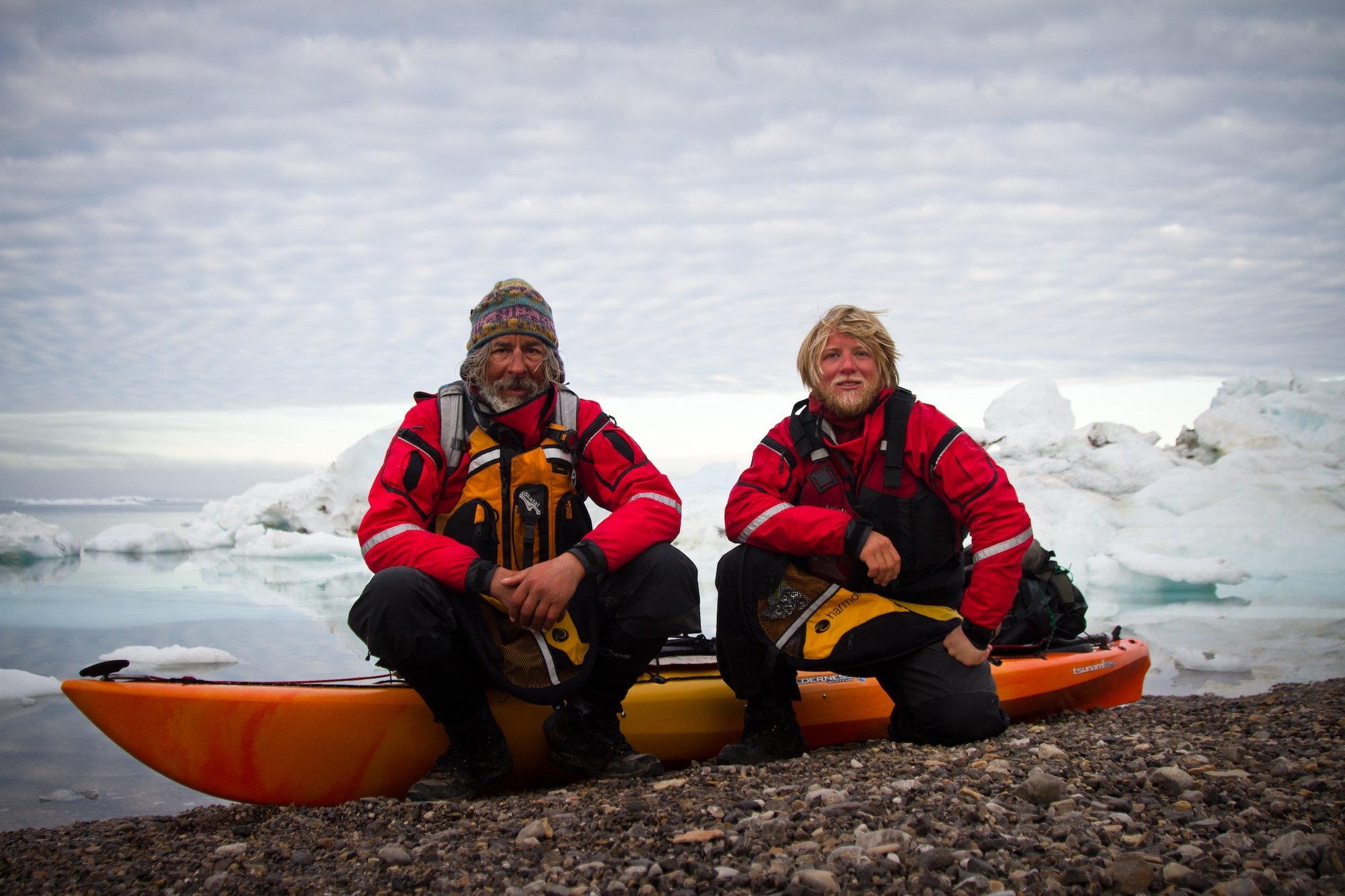 two wind-chapped men pose on a kayak in the Arctic