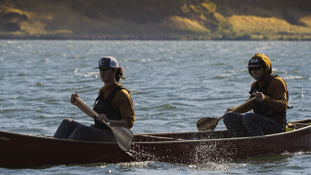 two young men paddle a canoe in light chop