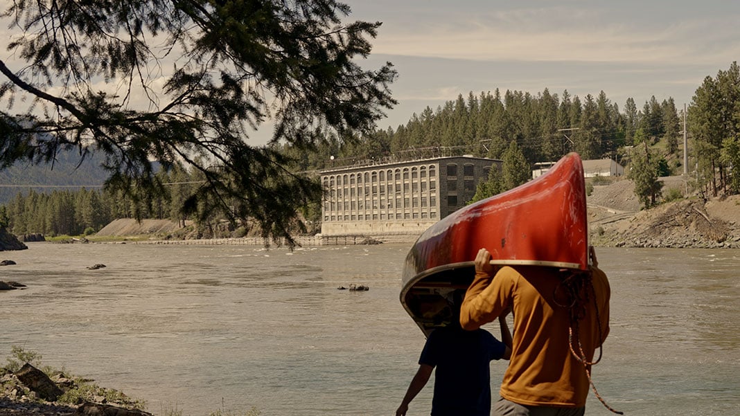 two people portage a canoe near buildings on the Columbia River