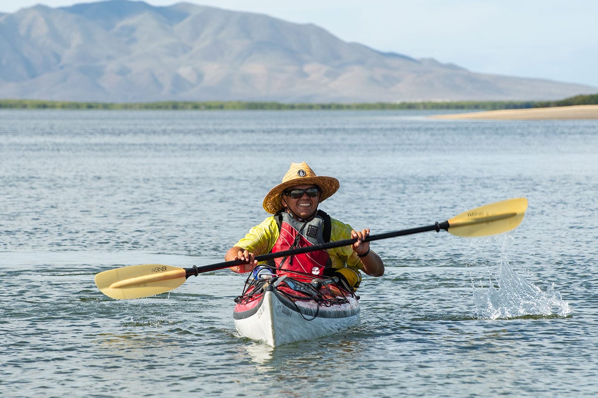 a man smiles as he paddles his sea kayak in the sun