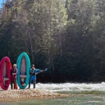 Inflatable Kayak Review: AIRE’s Spud & Tater two women kayakers pose by the water with AIRE's Spud and Tater inflatable whitewater kayaks