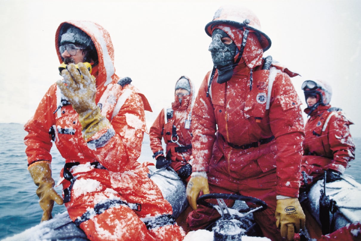 Coastal professionals dressed in Mustang Survival gear on boat covered with snow in the 1980s.