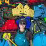 Best Life Jackets For 2025 Paddling Magazine editor-in-chief Kaydi Pyette holds a canoe paddle while wearing and surrounded by a selection of her picks for best life jackets